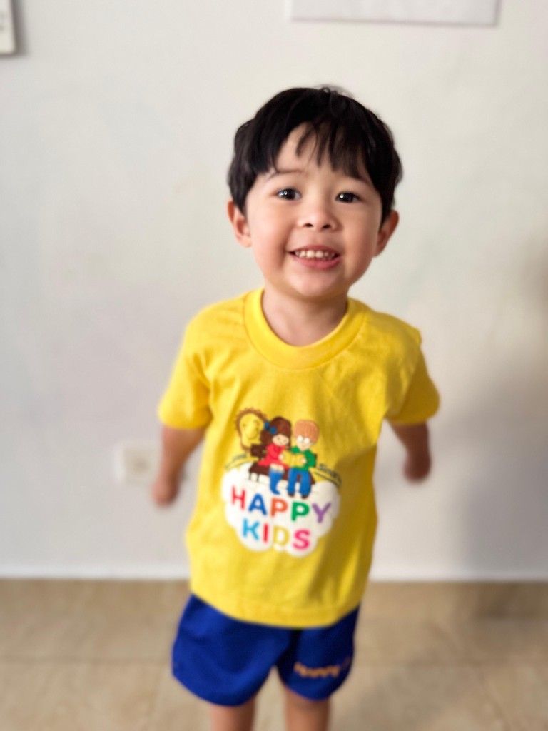 Boy in a yellow Happy Kids shirt smiling at the camera.
